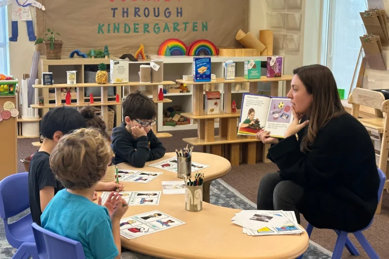 preschool teacher reading to four students sitting at a table